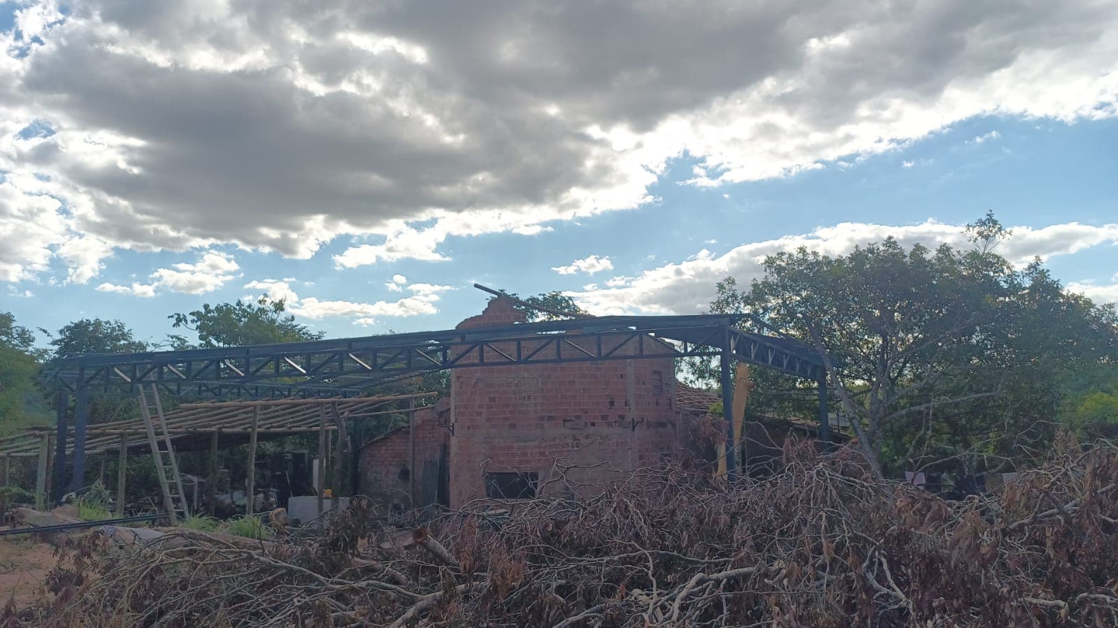 Frente da sede no início da transformação, com armação metálica do telhado em montagem e galhos no terreno.